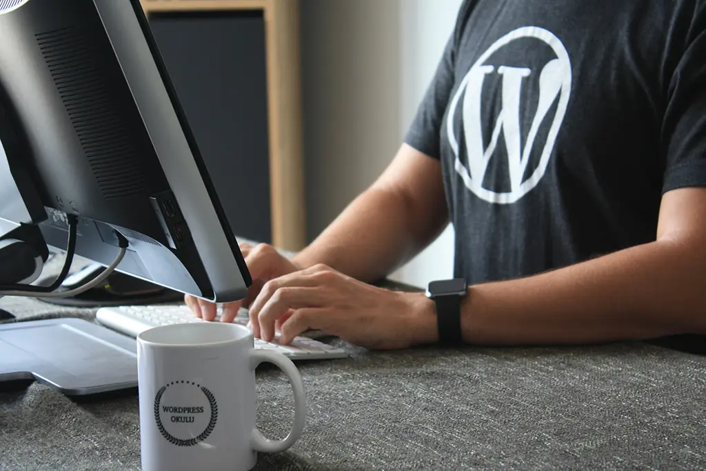 A remote WordPress developer wearing a shirt is typing in the keyboard and creating a website for a business